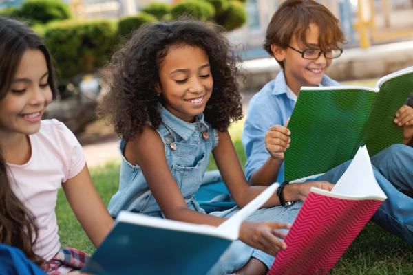 three school-aged children reading together outside