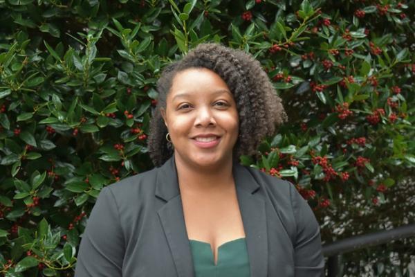 woman with should-length curly hair stands in front of large green shrub and smiles at camera; sherra lawrence