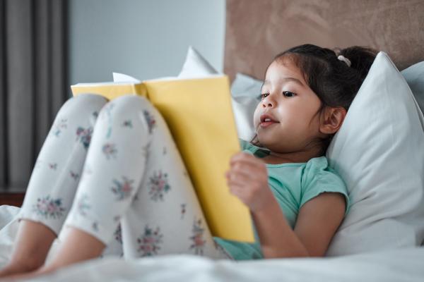 young girl sitting up in bed reading a picture book