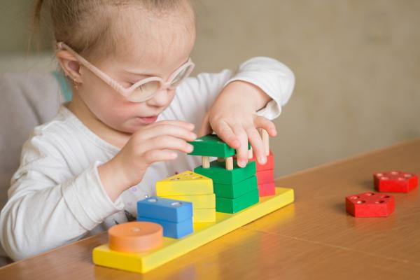 young girl with blond hair and glasses with Down syndrome sorts geometric shapes