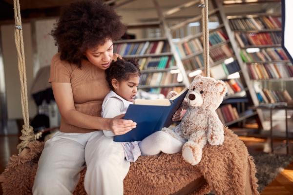 mother reads book to young daughter and her stuffed bear