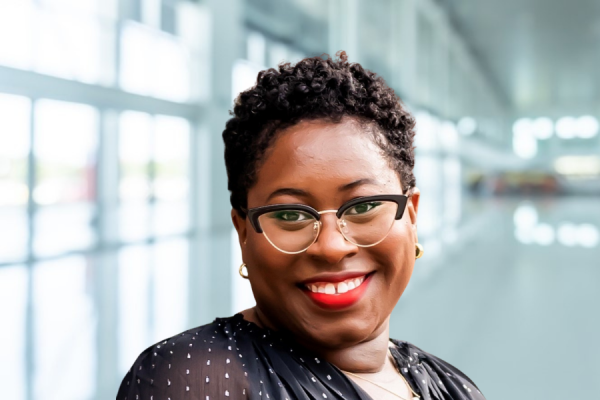 tamara robertson; african-american woman with short brown hair and cat-eye shaped glasses stands in light-filled hallway