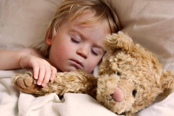 blond haired toddler napping with large tan teddy bear
