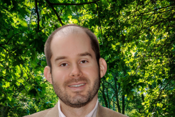 Will Aldridge headshot - man with beard wearing white shirt and tan jacket smiling at camera while standing outside in front of a tree