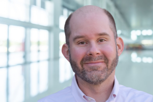 Will Aldridge; man with close-cropped mustache and beard wearing a pale pink shirt smiles at camera