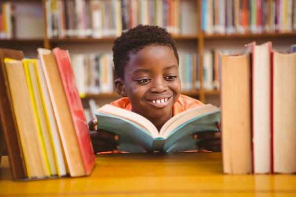 young boy reading in library surrounded by books