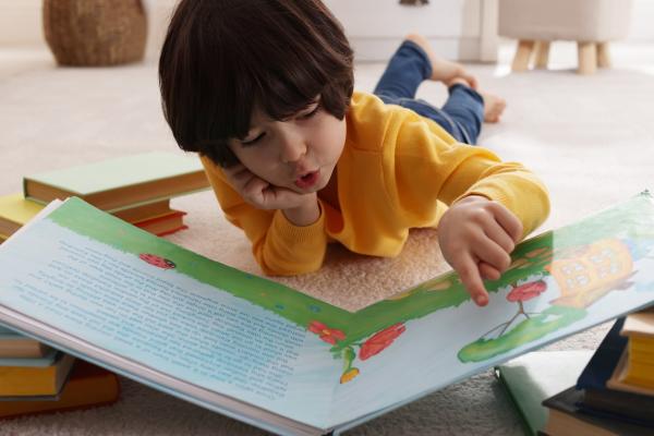 little boy reading book on floor at home