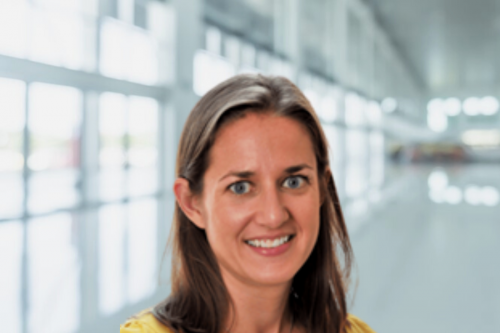 Becky Dees; woman with brown hair stands in brightly lit office hallway